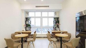 Un comedor con mesas y sillas redondas, un ventanal con vistas a la ciudad y una zona de cocina con estufa.
