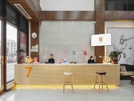 Mostrador de recepción de hotel con un cartel grande con el número 7, un reloj y una zona de espera con dos sillas.