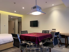 Habitación de hotel con cama, una mesa con sillas, televisor de pantalla plana y aire acondicionado instalado en el techo.