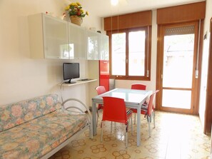A small living area with a sofa, a dining table with chairs, a television, and a window with a view. - First-floor Accommodation in Residence With Pool (San Michele al Tagliamento)
