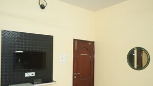 A room with a television mounted on a textured wall, a wooden door, and a round mirror on the wall. - Hotel Shree Banaras (Varanasi)