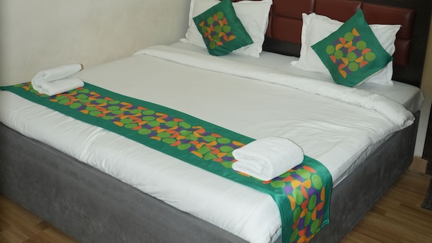 A neatly made bed with white linens and a green patterned bed runner. - Hotel Shree Banaras (Varanasi)
