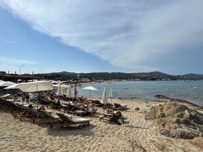 Ein Strand mit Liegestühlen und Sonnenschirmen, einem klaren Himmel und ruhiger See.