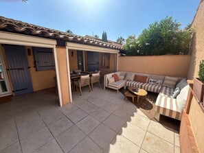 A covered patio area with a dining table and chairs, a striped sofa, and a small table. - Cozy 2-bedroom apartment, with a terrace, 10 meters from Nartelle Beach (Sainte-Maxime)