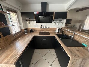 A modern kitchen with a central island, black cabinets, and a large window with blinds. - Cozy 2-bedroom apartment, with a terrace, 10 meters from Nartelle Beach (Sainte-Maxime)