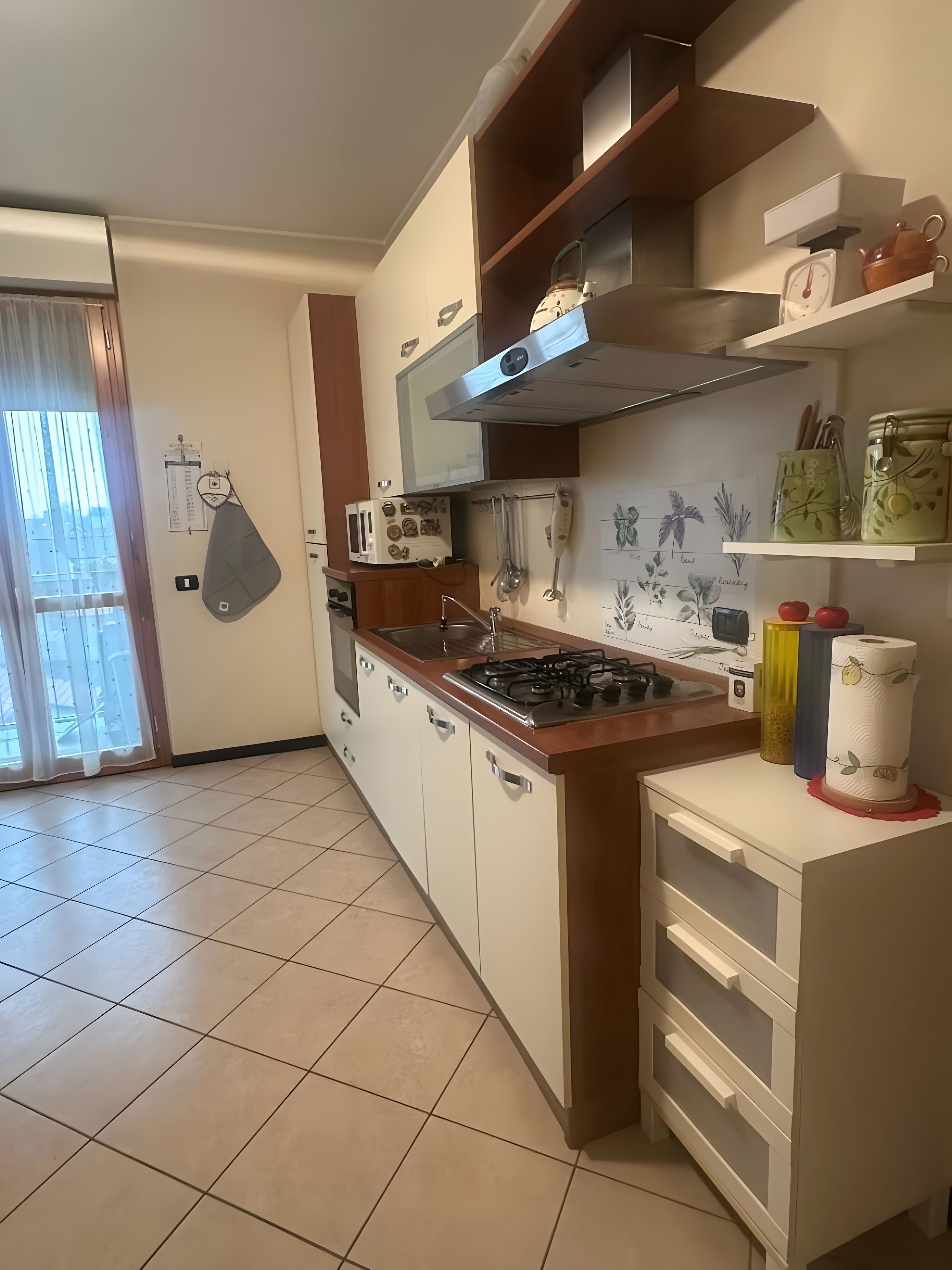 Una cocina con estufa, microondas y ventana con cortinas.