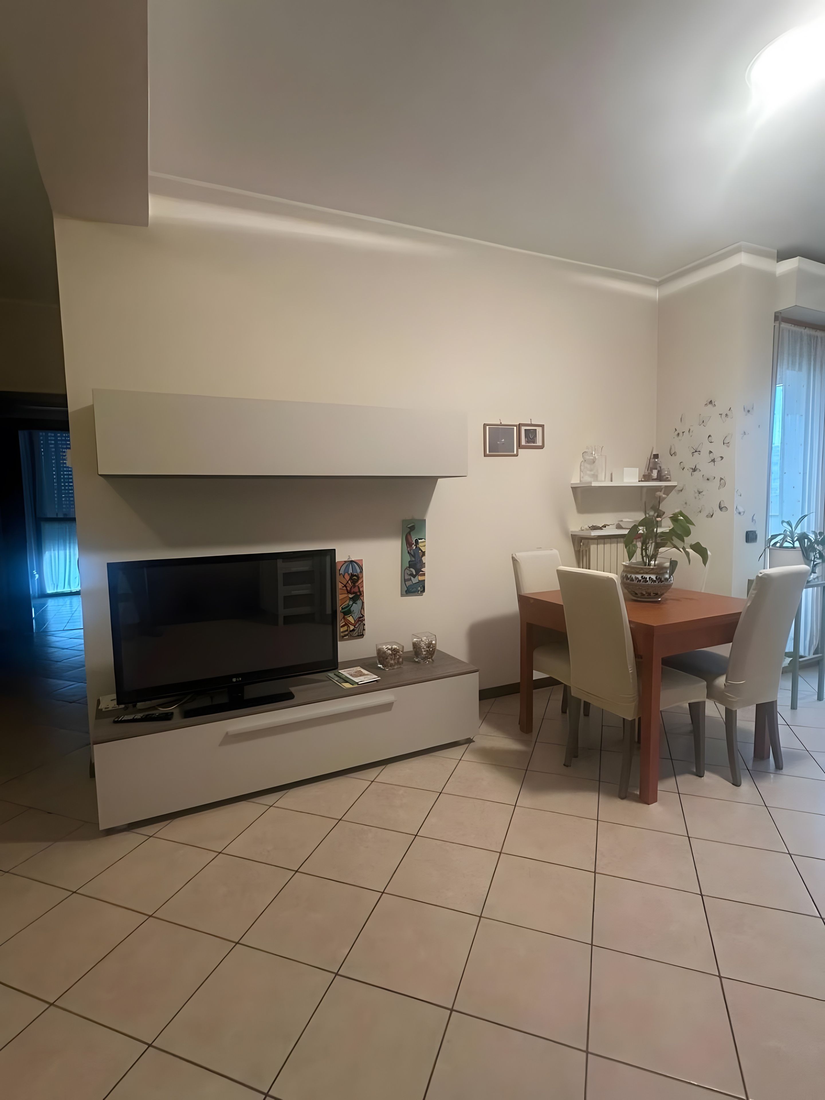 Una sala moderna con un televisor de pantalla plana, una mesa de comedor con sillas y una zona de cocina con estantes.