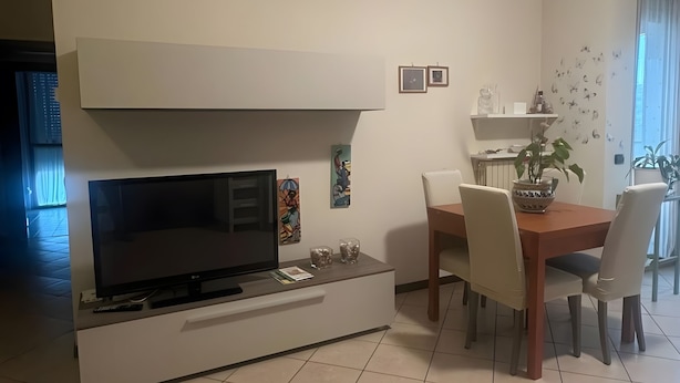 Een moderne woonkamer met een flatscreen televisie, een eettafel met stoelen en een keukenhoek met een plank.