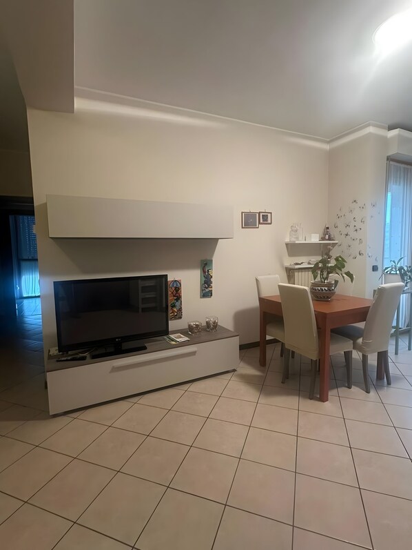 Un saló modern amb televisió plana, taula de dinar amb cadires i zona de cuina amb prestatgeria.