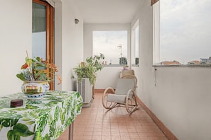 A balcony with a table, chairs, potted plants, and a view of the cityscape.
