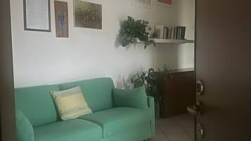 Una habitación con un sofá verde, una puerta y una estantería con libros y una planta.