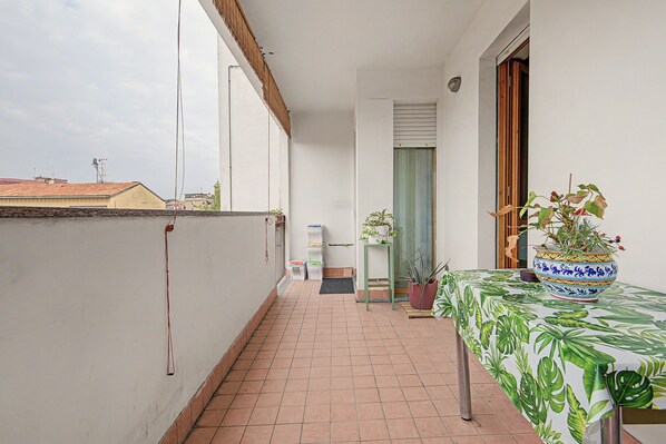 A narrow balcony with a tiled floor, a small table with a plant, and a door leading to an interior space.