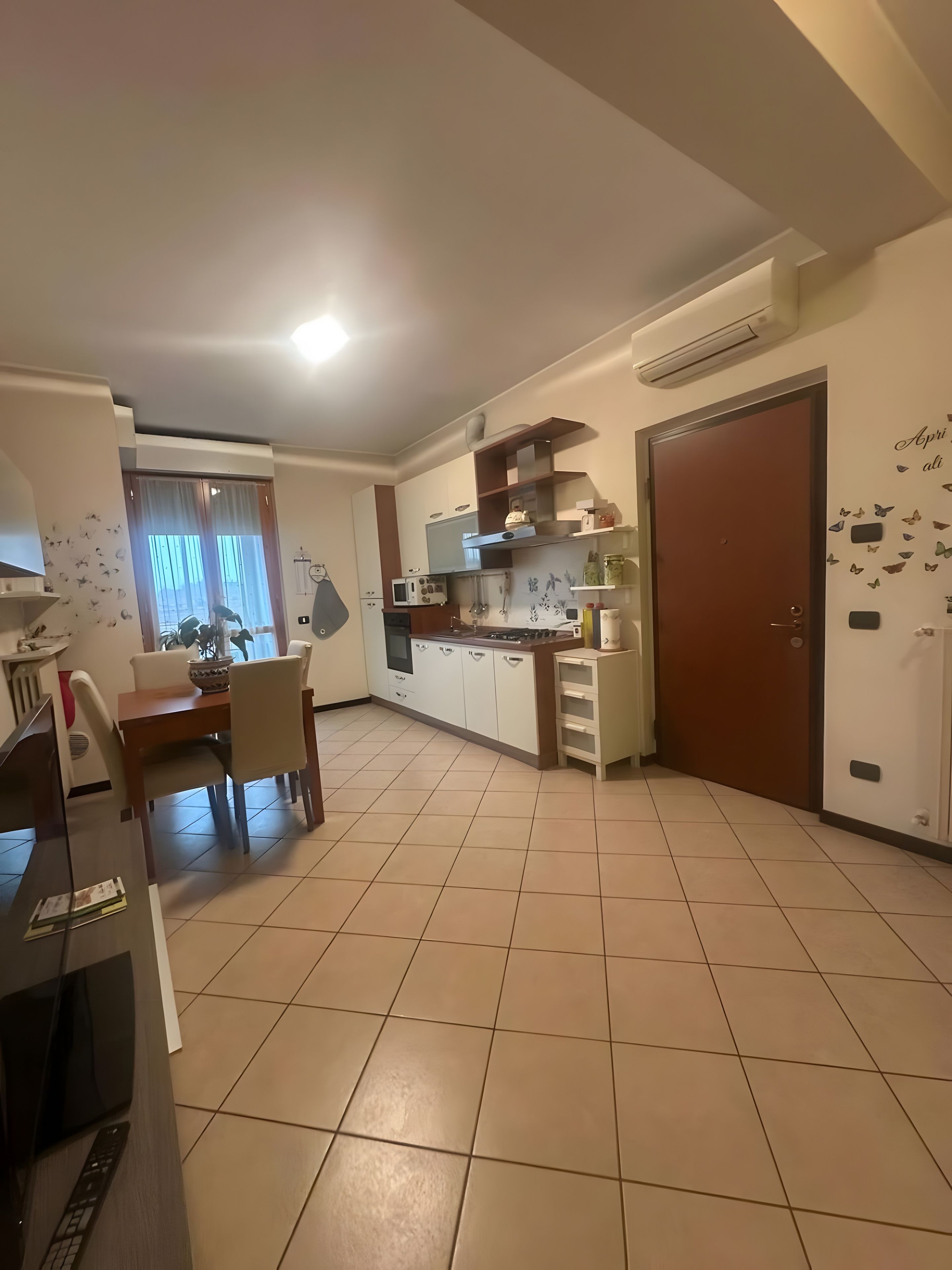 Una cocina moderna con armarios blancos, una mesa de comedor con sillas y un gran ventanal con un dibujo de mariposa.