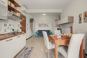 A modern kitchen with white cabinets, a dining table with chairs, and a living area with a sofa.