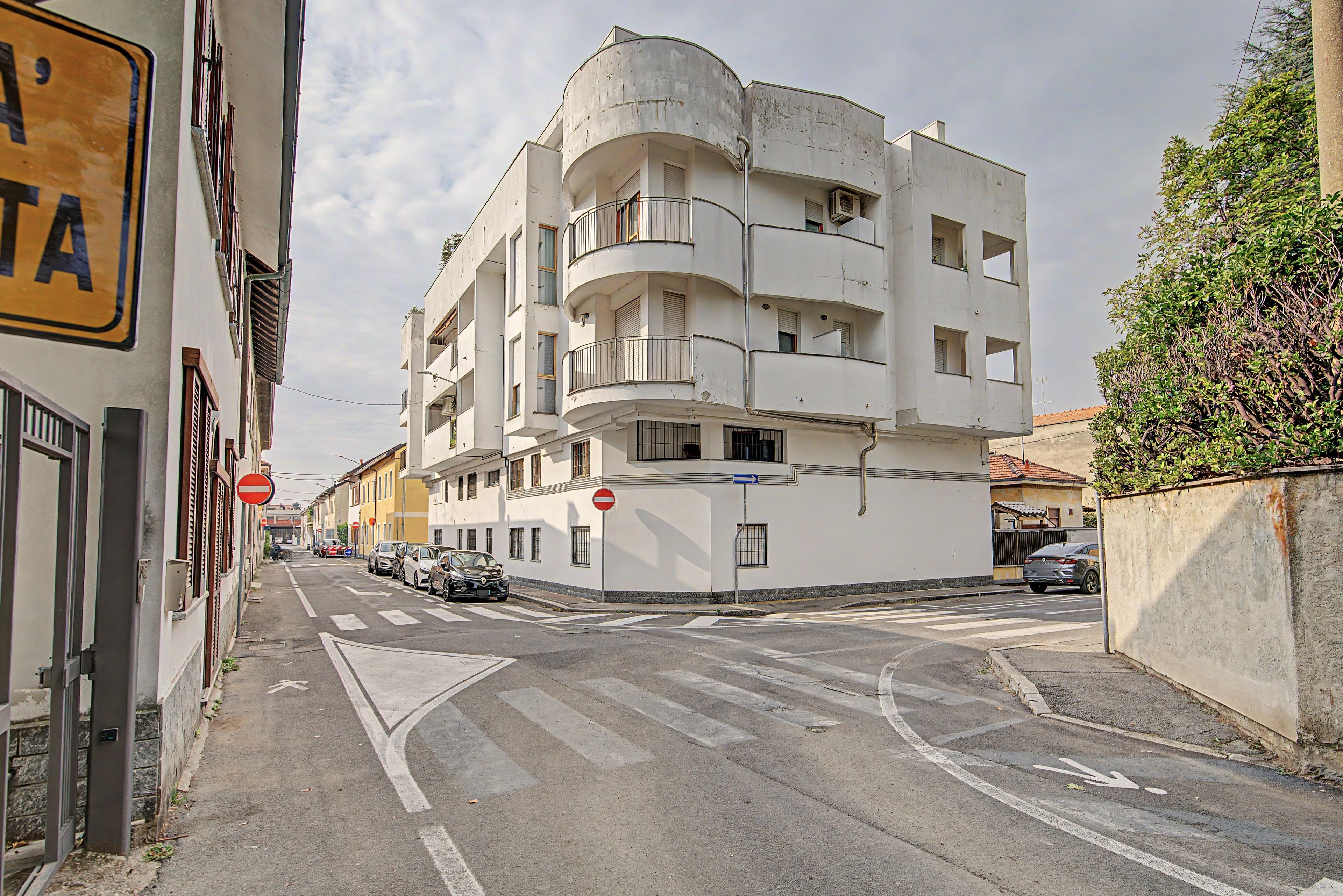 Un immeuble à plusieurs étages doté de balcons, un panneau indiquant l’interdiction d’accès et des voitures garées dans la rue.