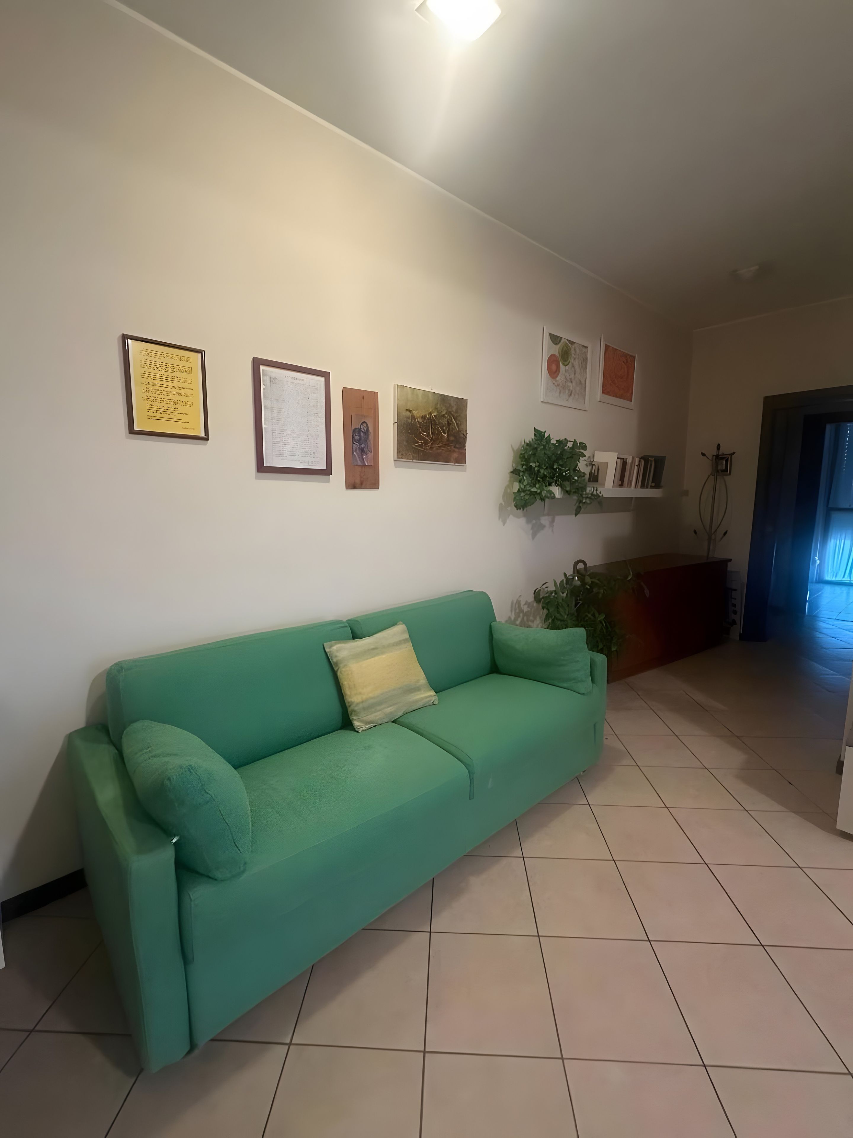 A living room with a green sofa, a wall-mounted shelf with books, and a door leading to another room.