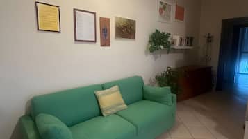 A living room with a green sofa, a wall-mounted shelf with books, and a door leading to another room.