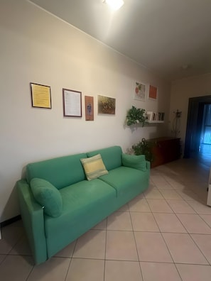 A living room with a green sofa, a wall-mounted shelf with books, and a door leading to another room. - Apartment 'Casalba Crossroads Milan Como Monza' with terrace, Wi-Fi and air conditioning (Bovisio-Masciago)