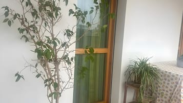 Um vaso de planta em vaso azul sobre piso de azulejos, porta de madeira com cortina verde, e uma mesa com toalha de mesa estampada.