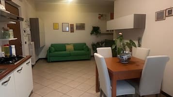 Una cocina con comedor, un sofá verde y una planta en maceta sobre la mesa.