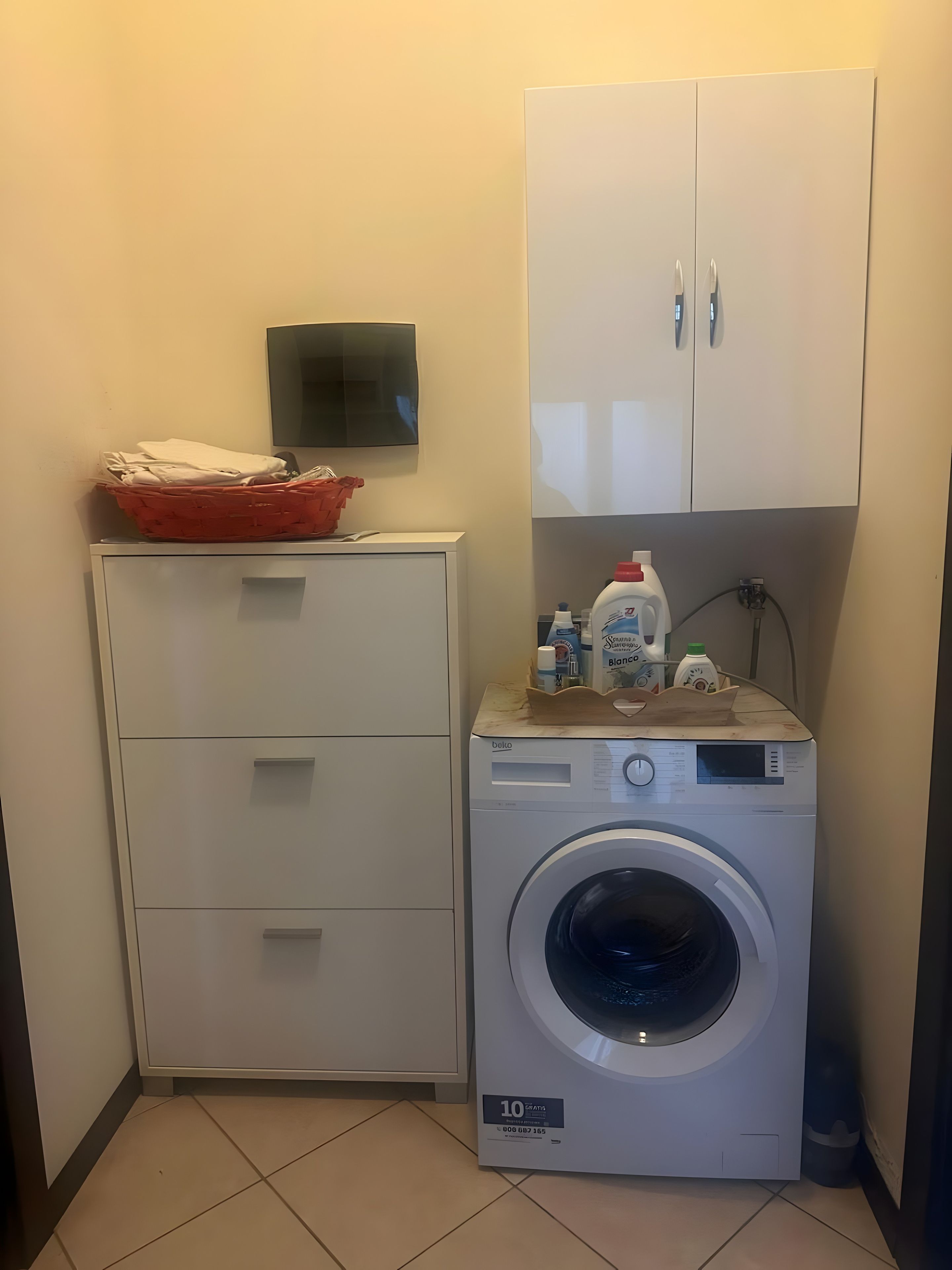 Uma lavanderia com máquina de lavar, um armário e uma televisão fixada na parede.