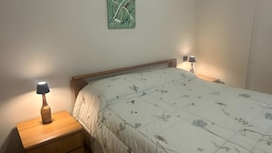 Een slaapkamer met een bed, twee nachtkastjes, een lamp en een abstract schilderij aan de muur.