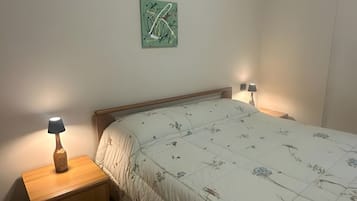 Un dormitorio con cama, dos mesitas de noche, una lámpara y un cuadro abstracto colgado en la pared.