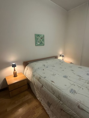 Un dormitori amb un llit, dues taules de nit, una tauleta auxiliar, una làmpada i un quadre abstracte penjat a la paret.