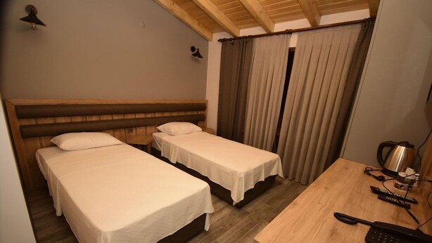 A hotel room with two single beds, a wooden desk with a telephone, and a curtain. - Koru Otel & Restaurant (Artvin)