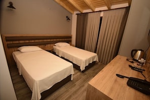 Een hotelkamer met twee enkele bedden, een houten bureau met telefoon en een gordijn.