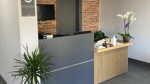 A reception area with a brick accent wall, a reception desk, a flat-screen TV, and a potted plant. - Koru Otel & Restaurant (Artvin)