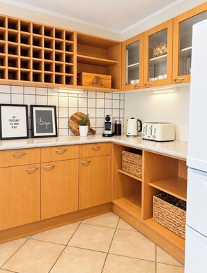 A kitchen with wooden cabinets, a tiled backsplash, and a white countertop. There are framed pictures, a coffee maker, and a toaster. - Gorgeous 7 bedroom beach villa in the heart of Oneroa (Waiheke Island)