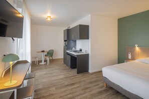 A compact hotel room with a kitchenette, a bed, a desk with a lamp, and a small dining area. - All Suites Appart Hotel Le Havre (Le Havre)