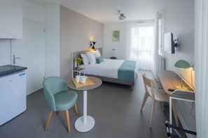 Habitación de hotel moderna con cama, escritorio, silla, mesita, armario y radiador.