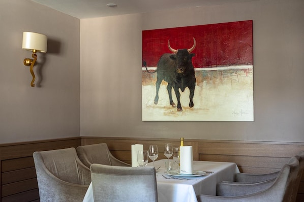 A dining area with a table set for two, a painting of a bull on the wall, and a wall-mounted light fixture. - Hotel Kaiserhof Medebach (Medebach)