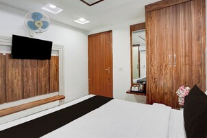 Un dormitorio con una cama, un armario de madera, un espejo, un ventilador de techo y un televisor en la pared.