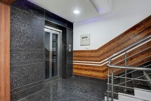 Un ascensor moderno con detalles metálicos, paneles de madera en la pared y una escalera de metal con barandilla.