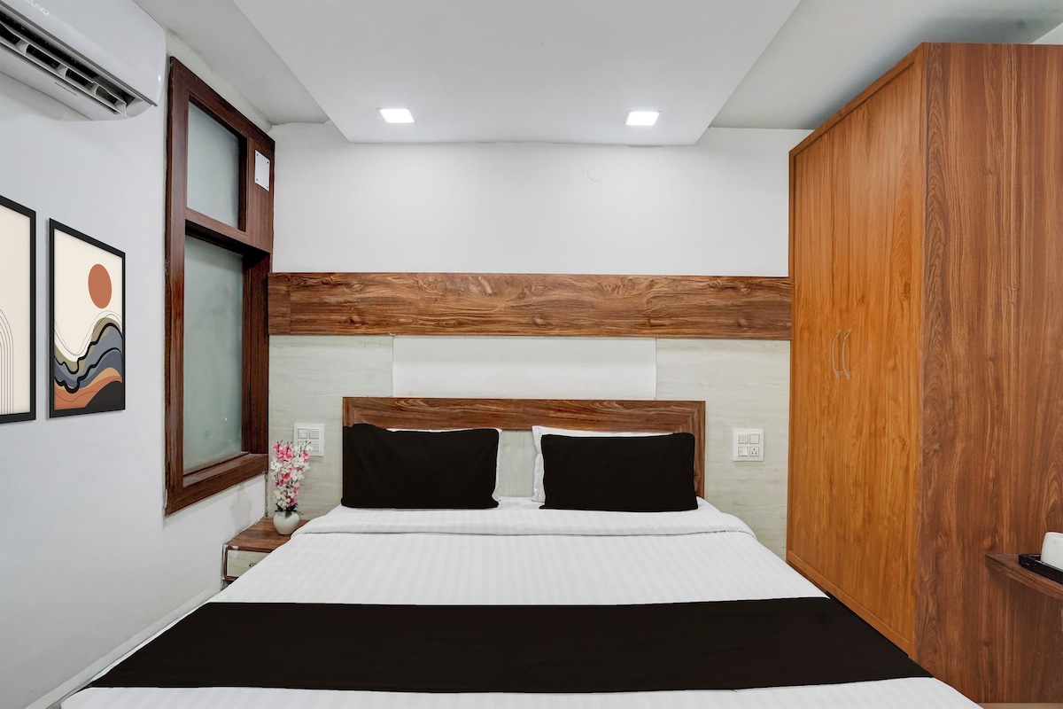 A bedroom with a bed, wooden headboard, two bedside tables, a nightstand, a wall-mounted air conditioner, and framed artwork.