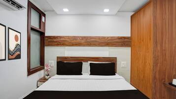 A bedroom with a bed, wooden headboard, two bedside tables, a nightstand, a wall-mounted air conditioner, and framed artwork.