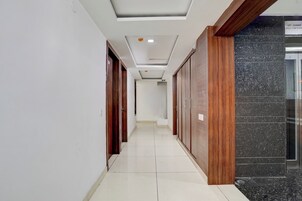 Un pasillo con puertas de madera y suelo de baldosas, que conduce a una zona de ascensores.