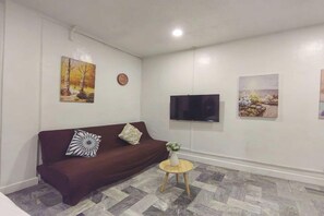 Ein Wohnzimmer mit einem braunen Sofa, einem runden Holztisch und zwei an der Wand hängenden Bildern.