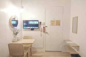 Ein Zimmer mit einem an der Wand befestigten Fernseher, einer Tür mit einem Schild, einem kleinen Tisch mit einem Stuhl und einer Mülltonne.