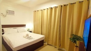 A hotel room with a bed, curtains, a television, and a small plant. - VG Pension and Residences by Zuzu (Cebu City)