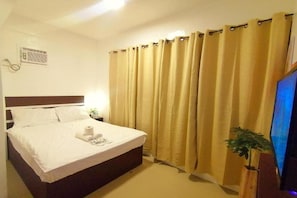 Ein Hotelzimmer mit Bett, Vorhängen, einem Fernseher und einer kleinen Pflanze.
