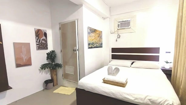 A hotel room with a bed, a potted plant, artwork on the walls, and a window with curtains. - VG Pension and Residences by Zuzu (Cebu City)