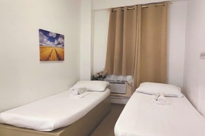 A hotel room with two single beds, a small table with a vase of flowers, and a painting of a field on the wall. - VG Pension and Residences by Zuzu (Cebu City)