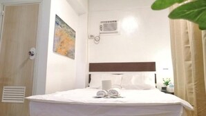 A hotel room with a bed, a wall-mounted air conditioning unit, a door, and a painting. - VG Pension and Residences by Zuzu (Cebu City)