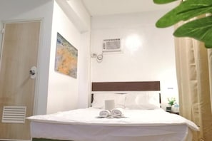 Ein Hotelzimmer mit einem Bett, einer Wand-Klimaanlage, einer Tür und einem Gemälde.