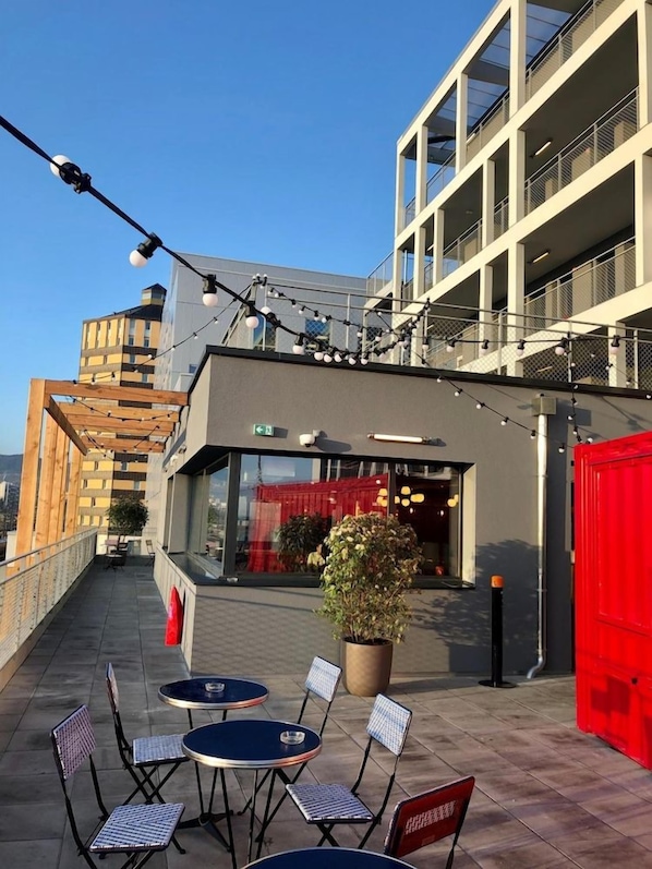 An outdoor seating area with tables and chairs, a potted plant, and a building with balconies and a red door. - Eklo Clermont Ferrand Centre Gare (Clermont-Ferrand)