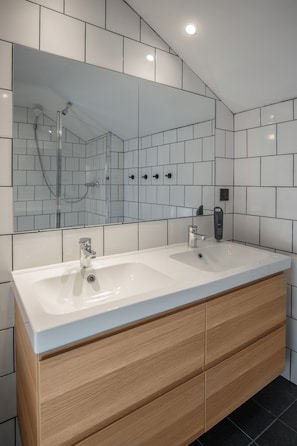 Ein modernes Badezimmer mit einem Doppelwaschbecken, Holzschränken und einem großen Spiegel.